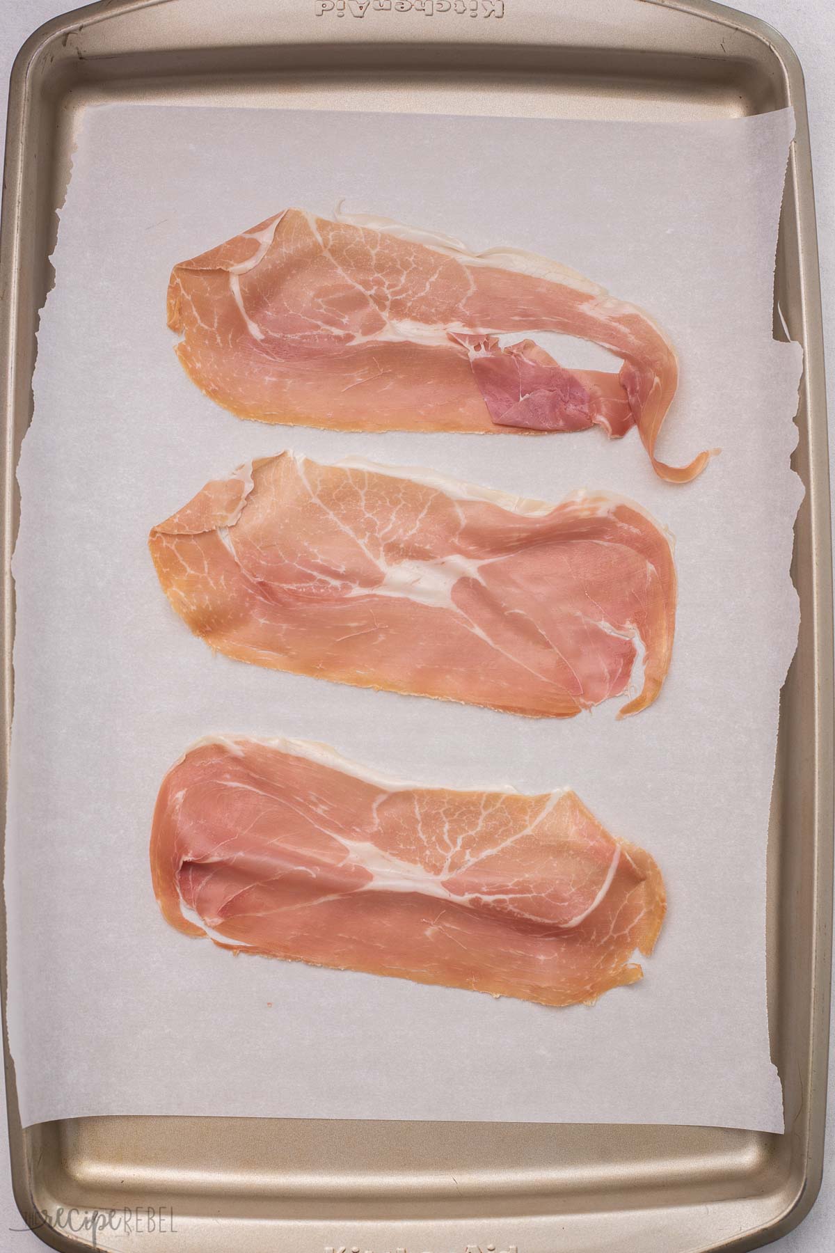 three slices of prosciutto lying flat on a baking sheet.