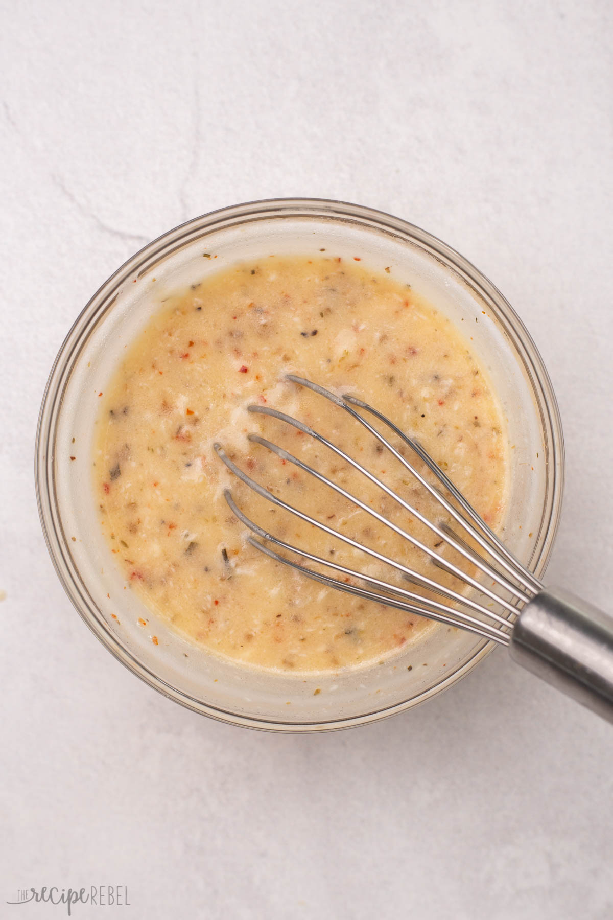 steel whisk in a glass bowl of sauce ingredients for tortellini pasta salad.