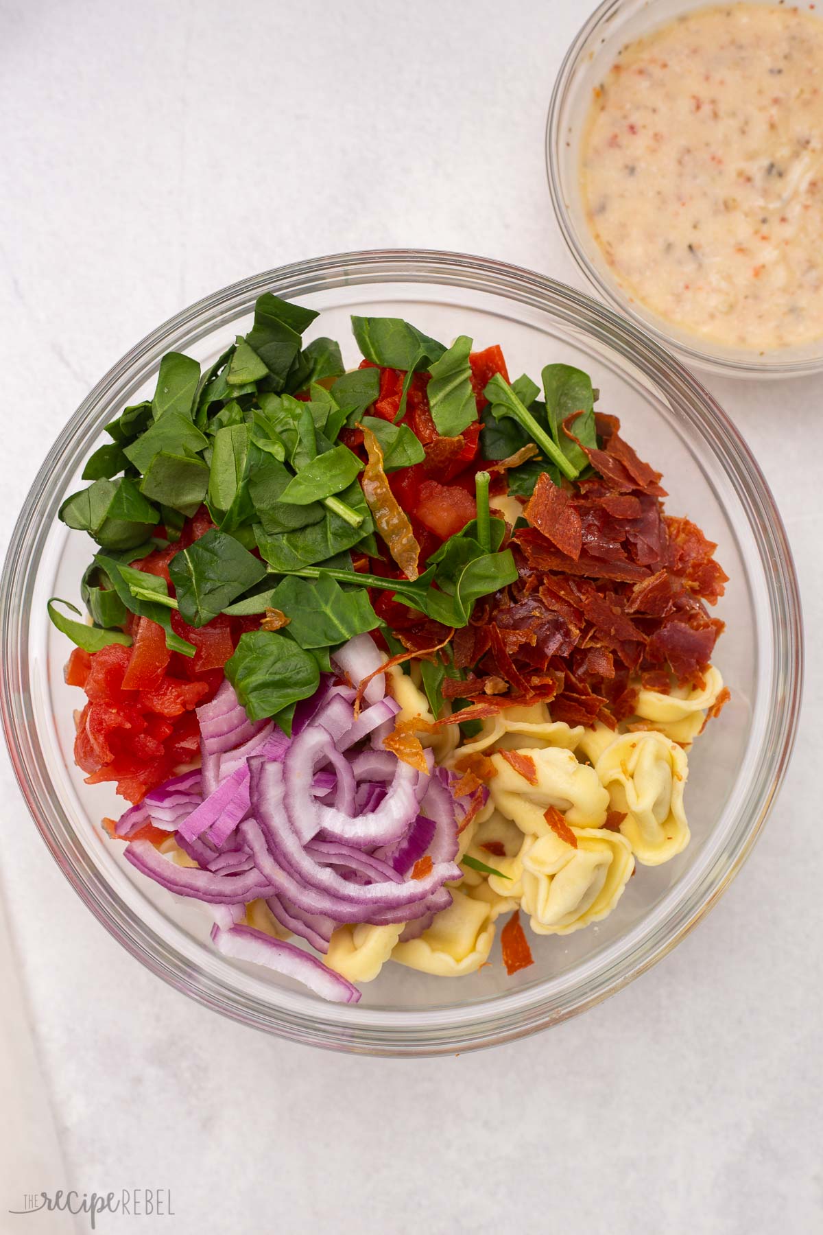 dry ingredients of tortellini pasta salad unmixed in a glass bowl.