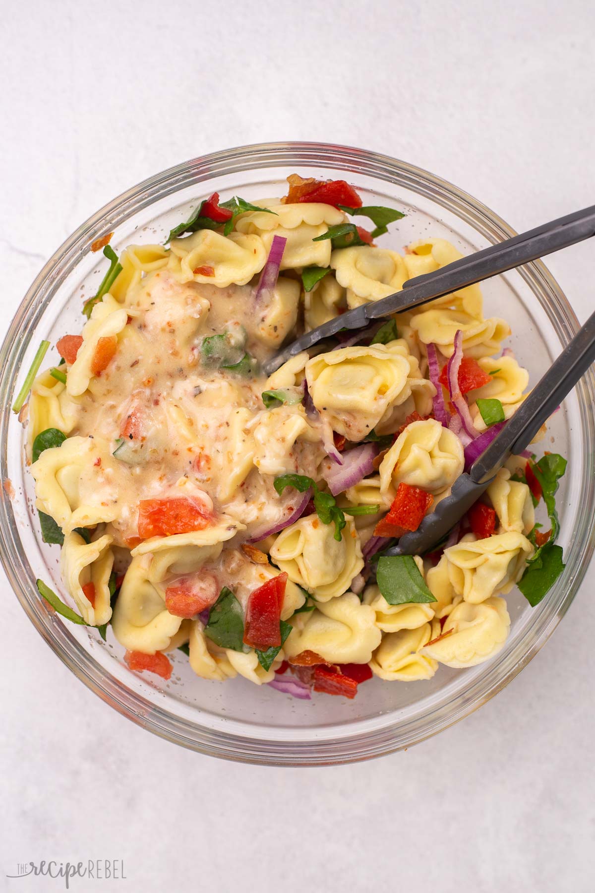 glass bowl of tortellini pasta salad with tongs in.