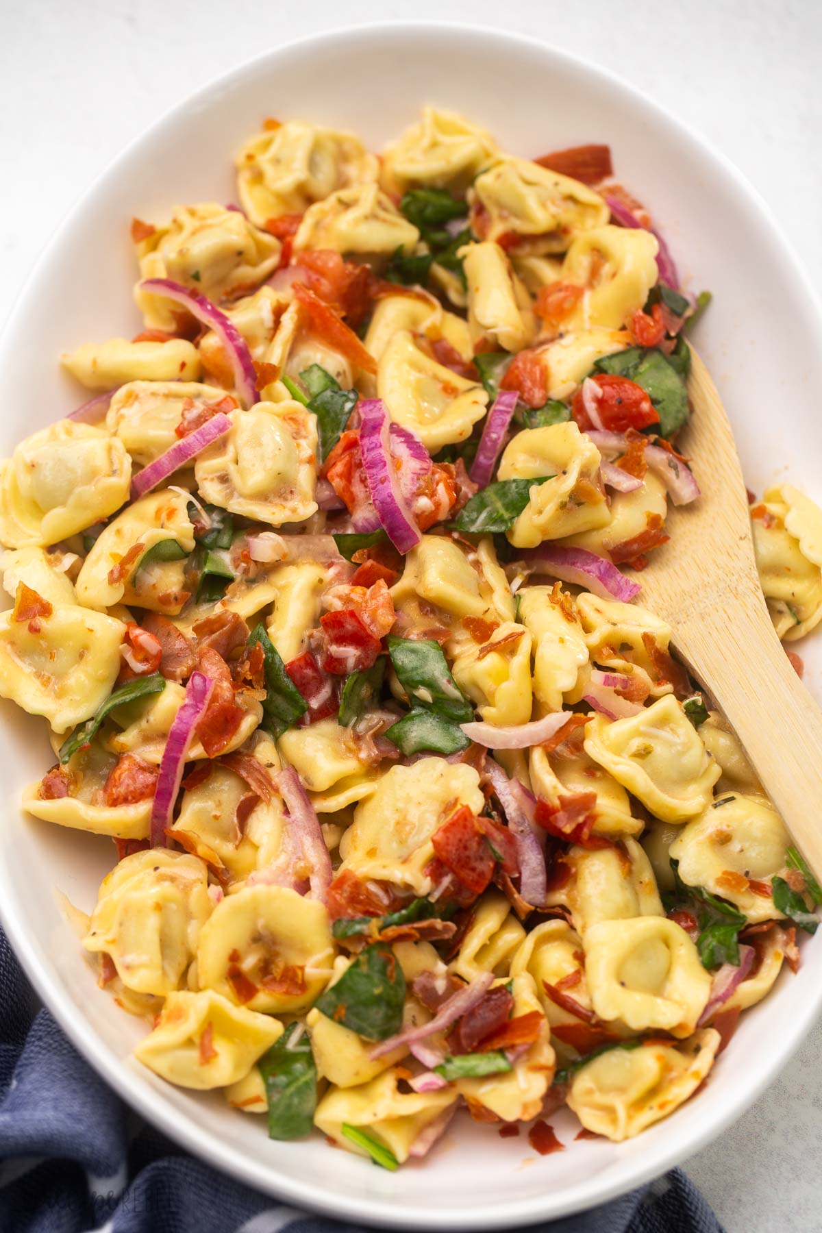 platter of tortellini pasta salad with wooden ladle in it.