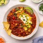 Top view of a bowl full of vegetarian chilli with chips and toppings around it.