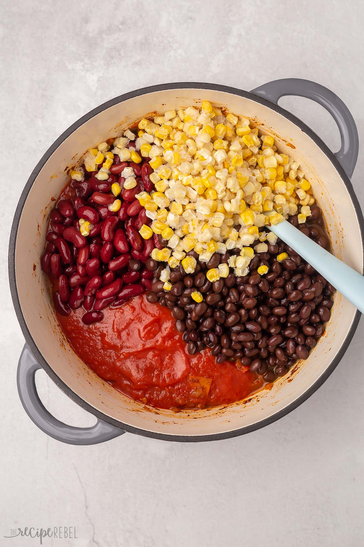 Top view of vegetables being added to vegetarian chilli in large grey pot.