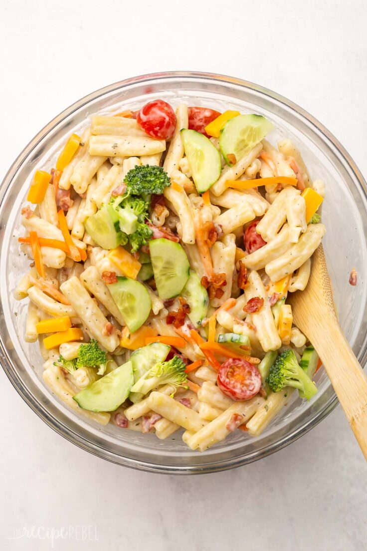 Top view of glass mixing bowl with Bacon Ranch Pasta Salad being mixed together with a wooden spoon. 