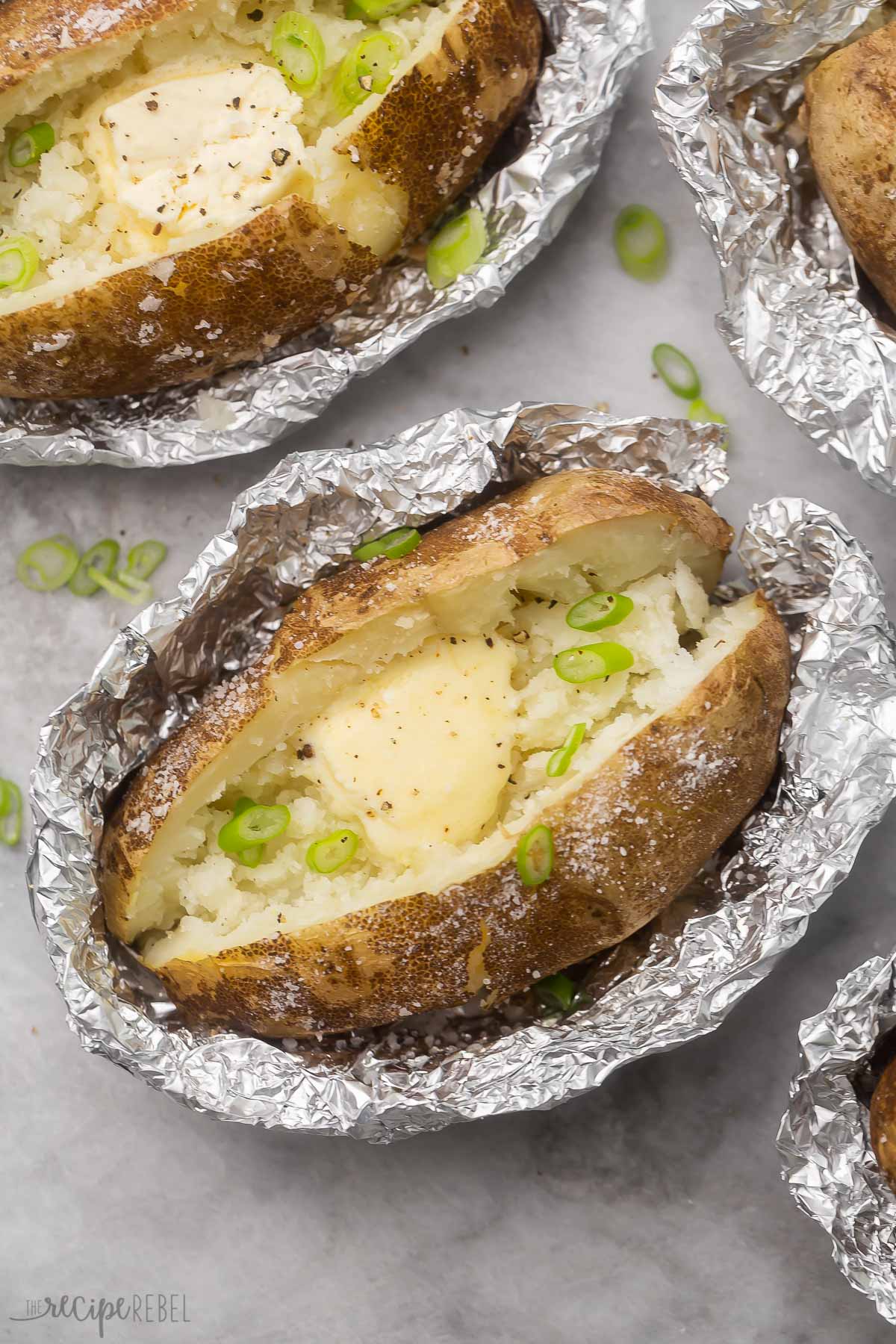 Top view of baked potato in a foil packet with butter in it and chopped green onions on top. 