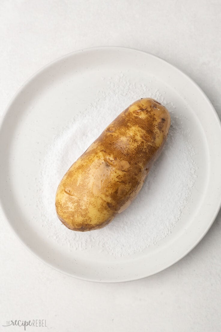 Top view of white plate with salt on it and a potato in the middle.  