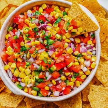 Top view of a big bowl of fresh corn salsa on a serving tray surrounded by tortilla chips.