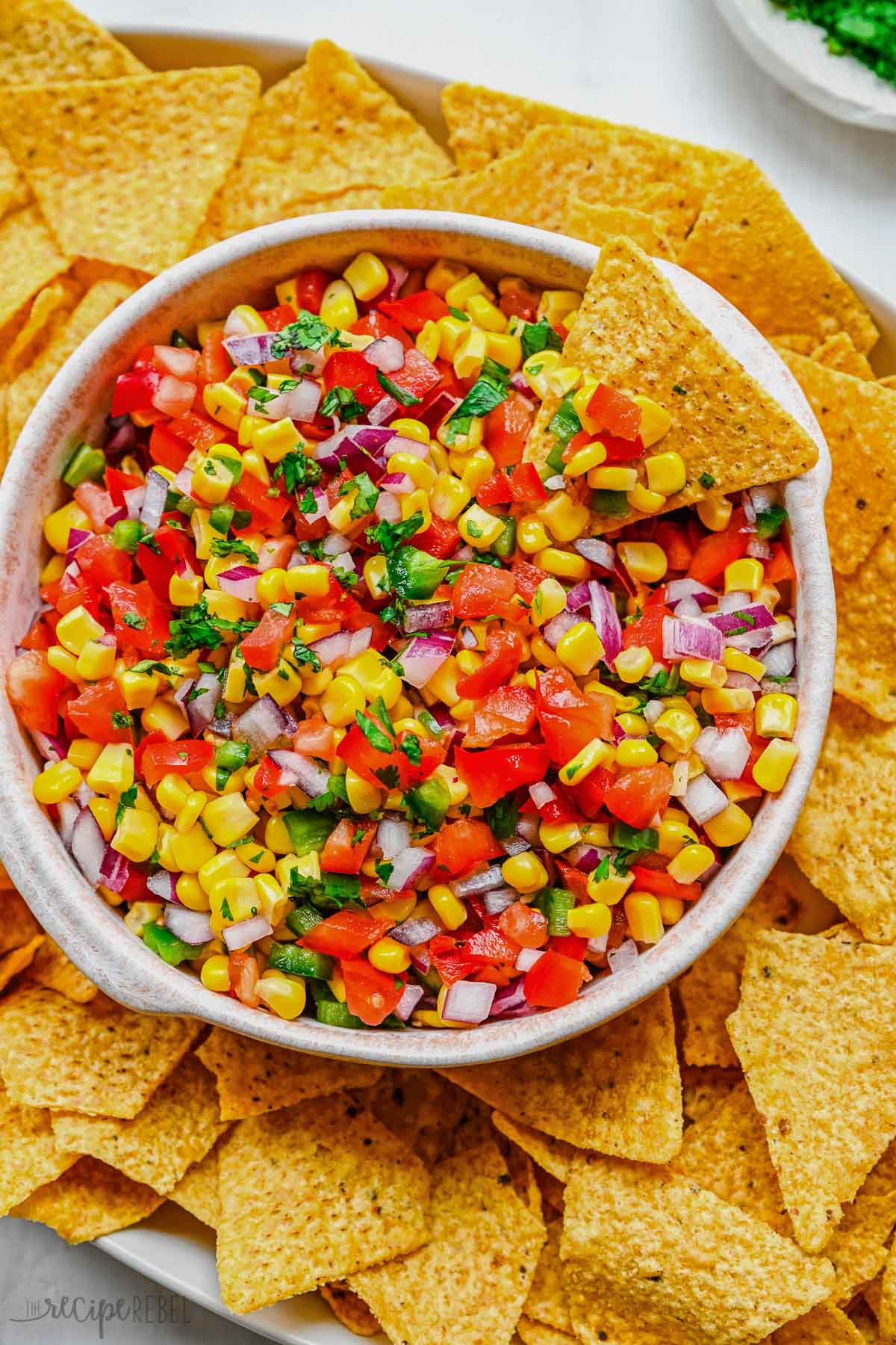 Top view of a big bowl of fresh corn salsa on a serving tray surrounded by tortilla chips.