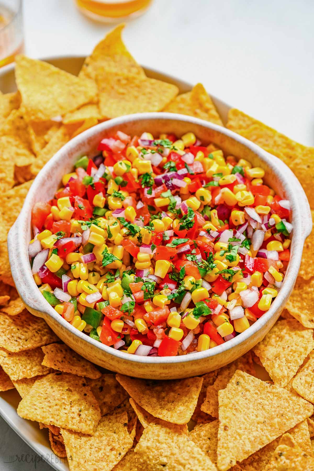 Top view of a big bowl of fresh corn salsa on a serving tray surrounded by tortilla chips.