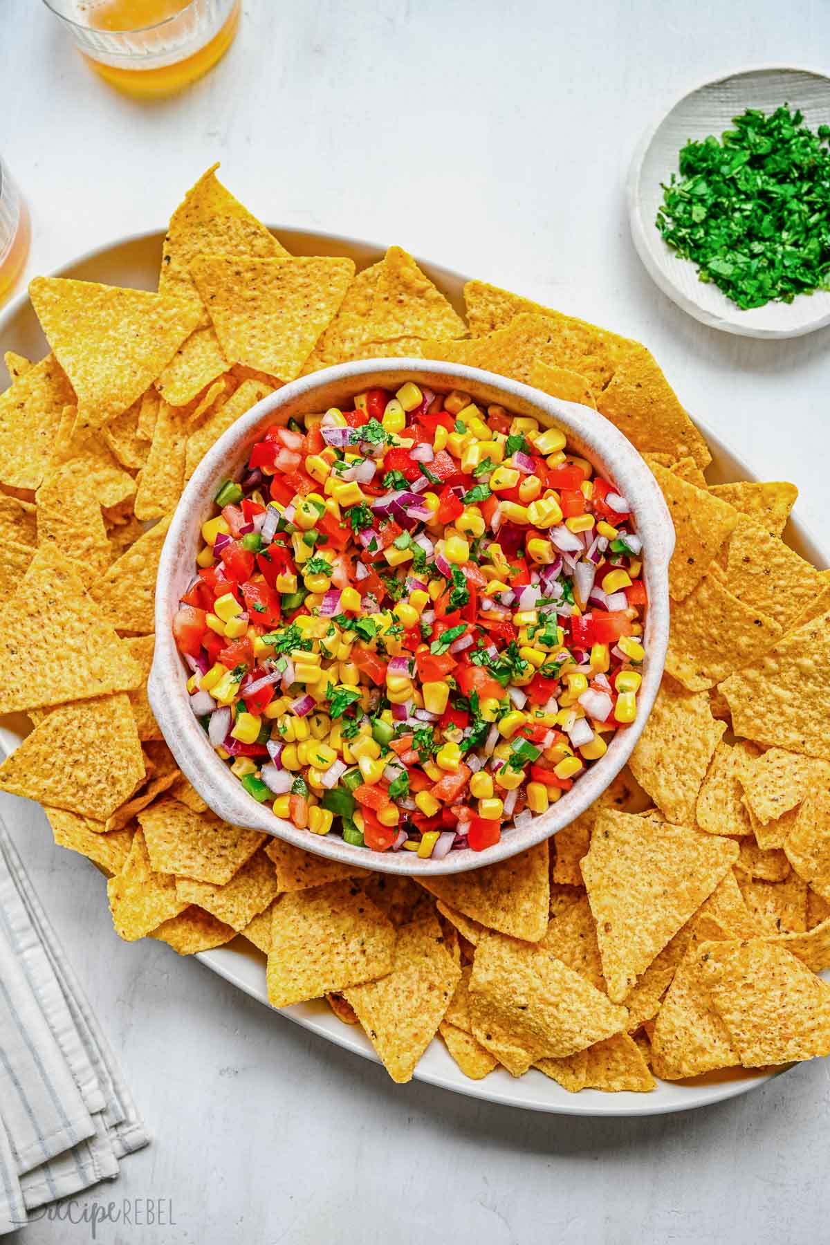 Top view of a big bowl of fresh corn salsa on a serving tray surrounded by tortilla chips.