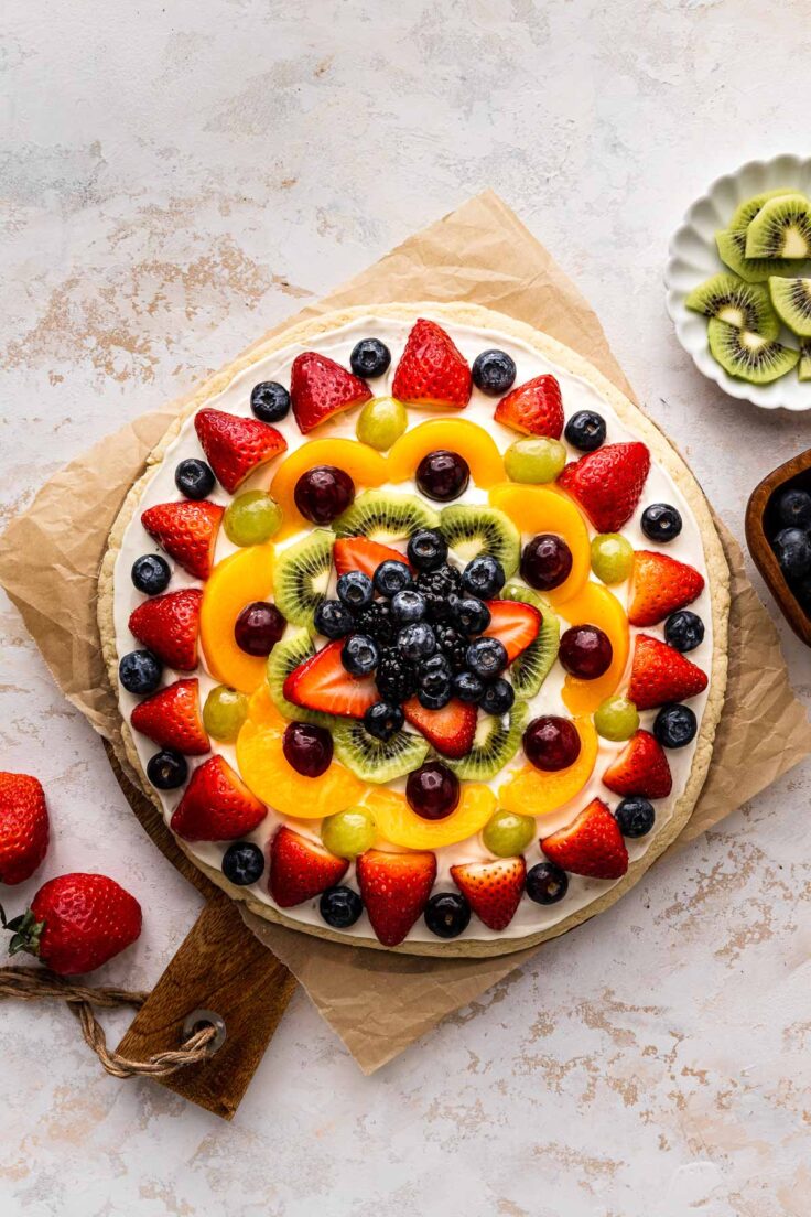 Top view of a colorful fruit pizza on a chopping board.