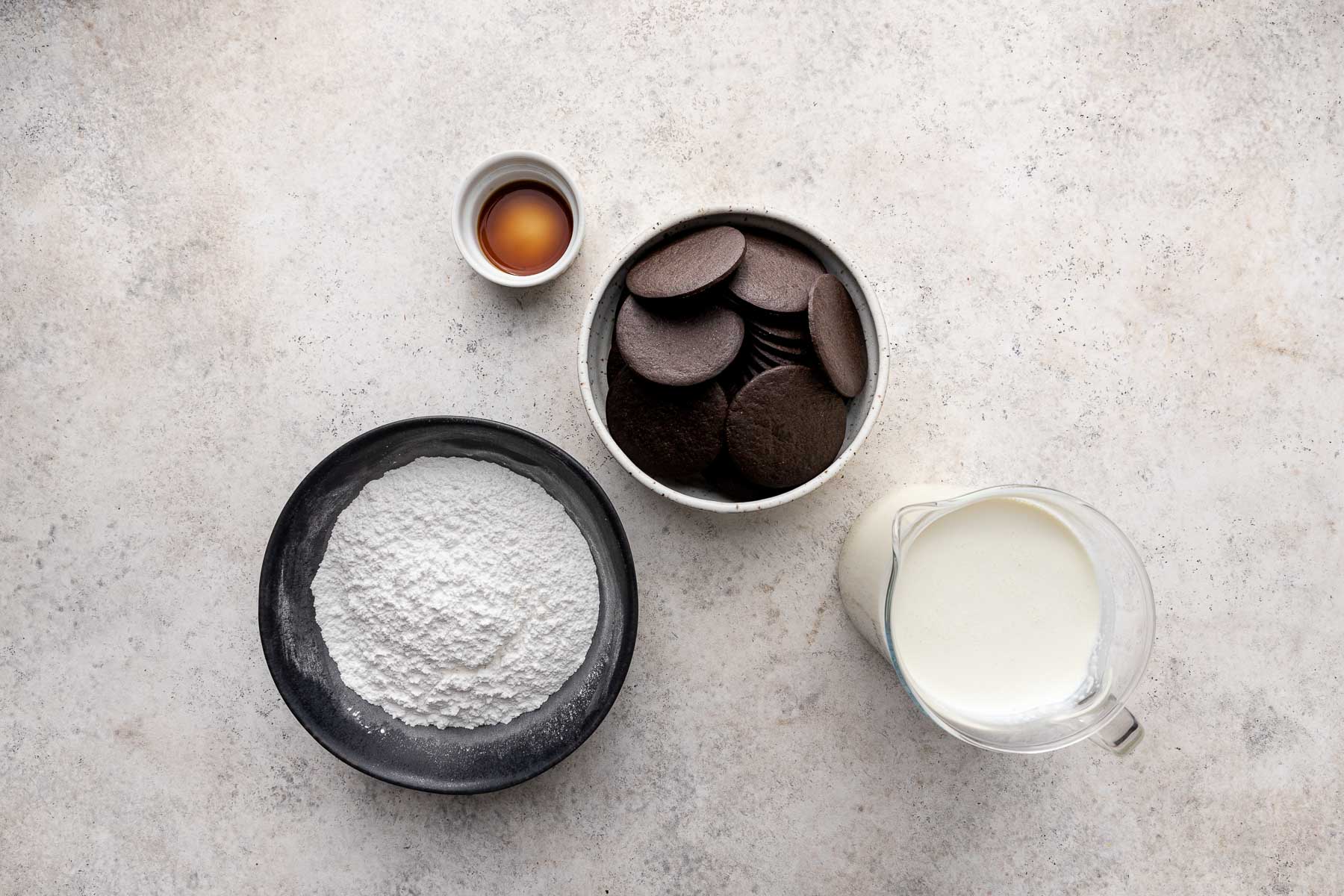 Top view of ingredients needed to make an ice box cake in small bowls on a gray surface. 