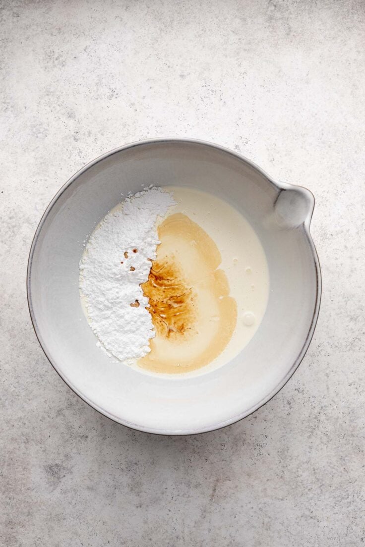 Top view of a mixing bowl with cream, sugar, and vanilla in it. 