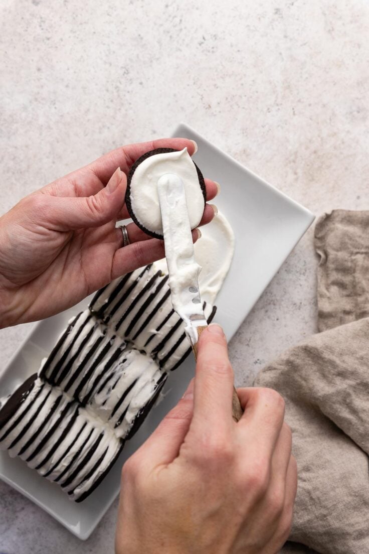 Top view of chocolate wafers being stuck together with whipped cream mixture and placed on a rectangle serving dish in a block. 