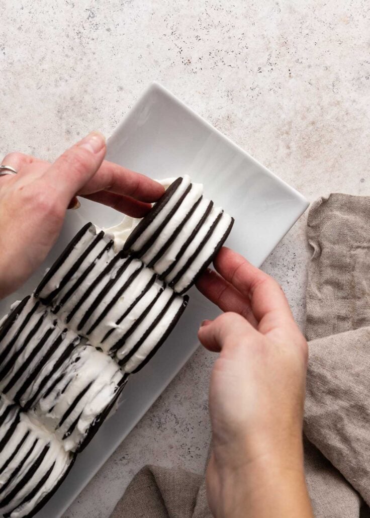 Top view of chocolate wafers being stuck together with whipped cream mixture and placed on a rectangle serving dish in a block. 