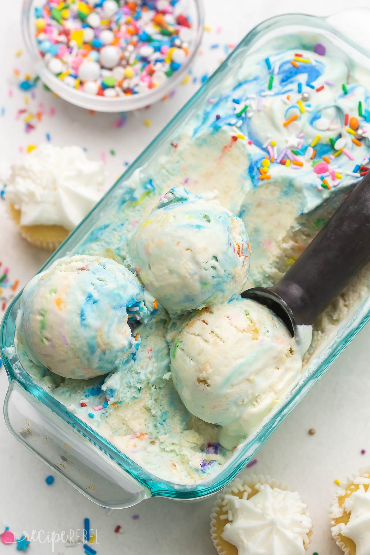 Top view close up of a glass dish filled with birthday cake ice cream with an ice cream scoop in it.