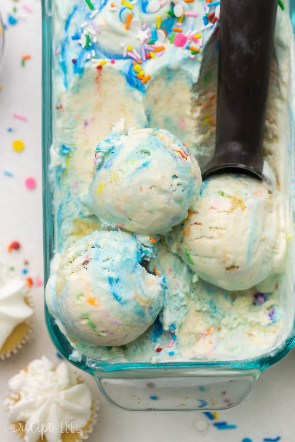 Top view of a glass dish filled with birthday cake ice cream with an ice cream scoop in it. 