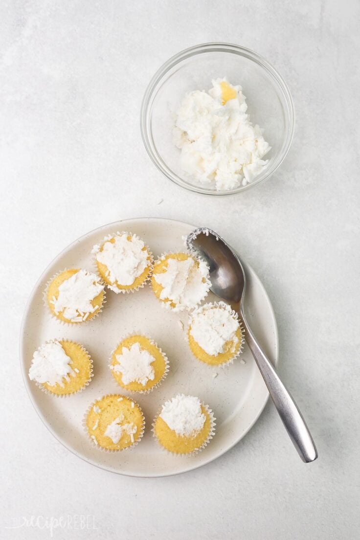 Top view of a plate of cuopcakes with frosting being scraped off into a small bowl.