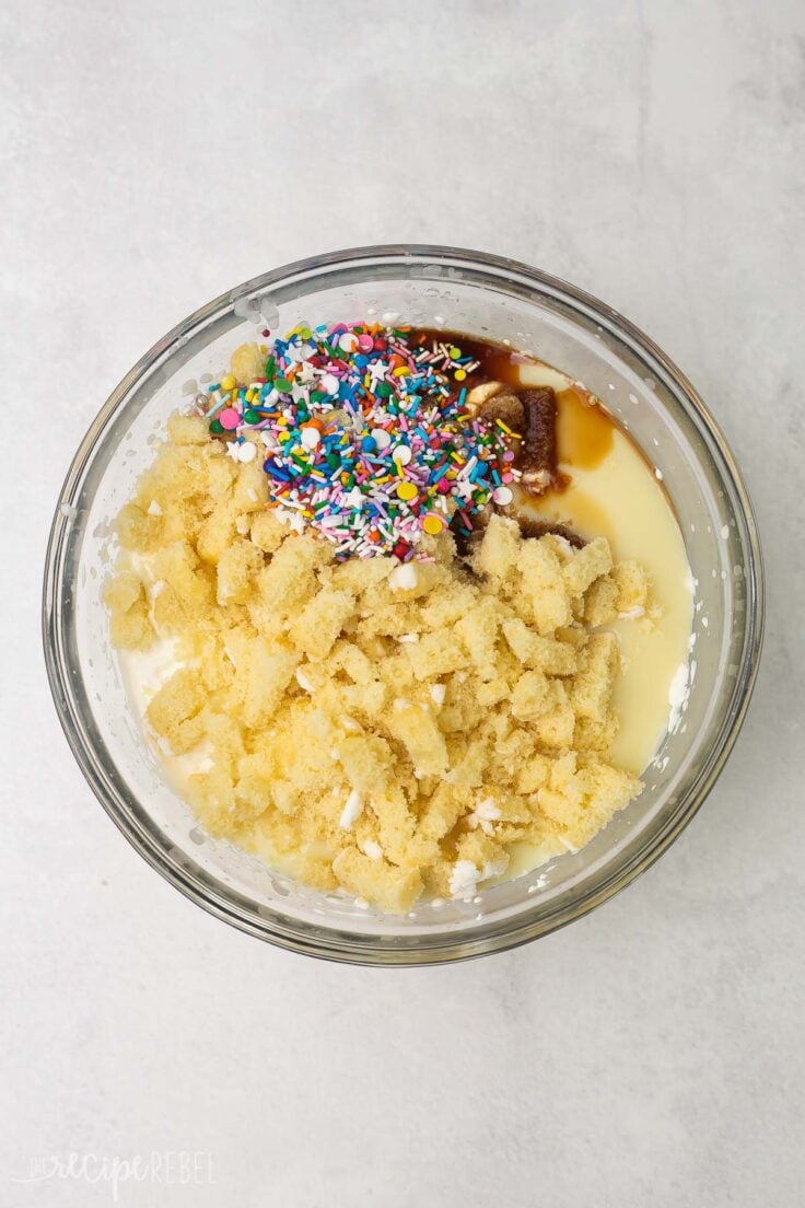 Top view of glass mixing bowl with a creamy mixture topped with crumbled cupcakes and sprinkles. 