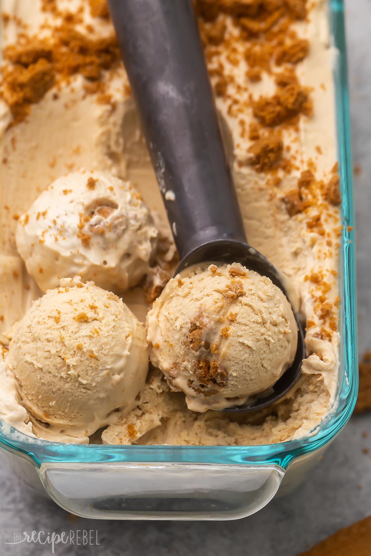 Top view of Biscoff ice cream in a glass dish with an ice cream scoop in it. 