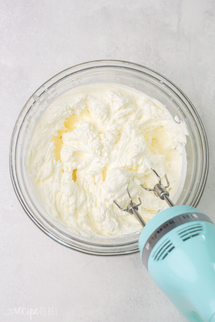 Top view of glass mixing bowl with creamy ingredients in it being whisked with a hand mixer. 