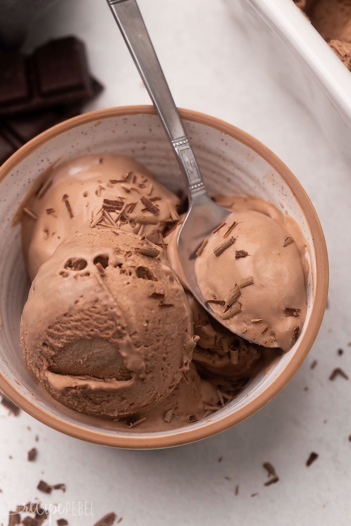 Top view of a bowl with scoops of chocolate ice cream in it with a spoon in it. 