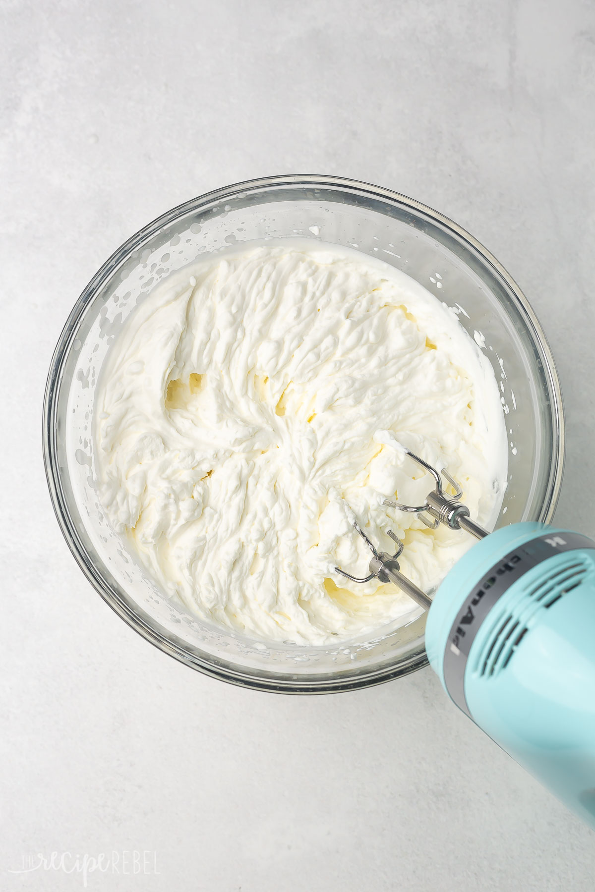 Top view of glass mixing bowl with creamy ingredients in it being whisked with an electric mixer.