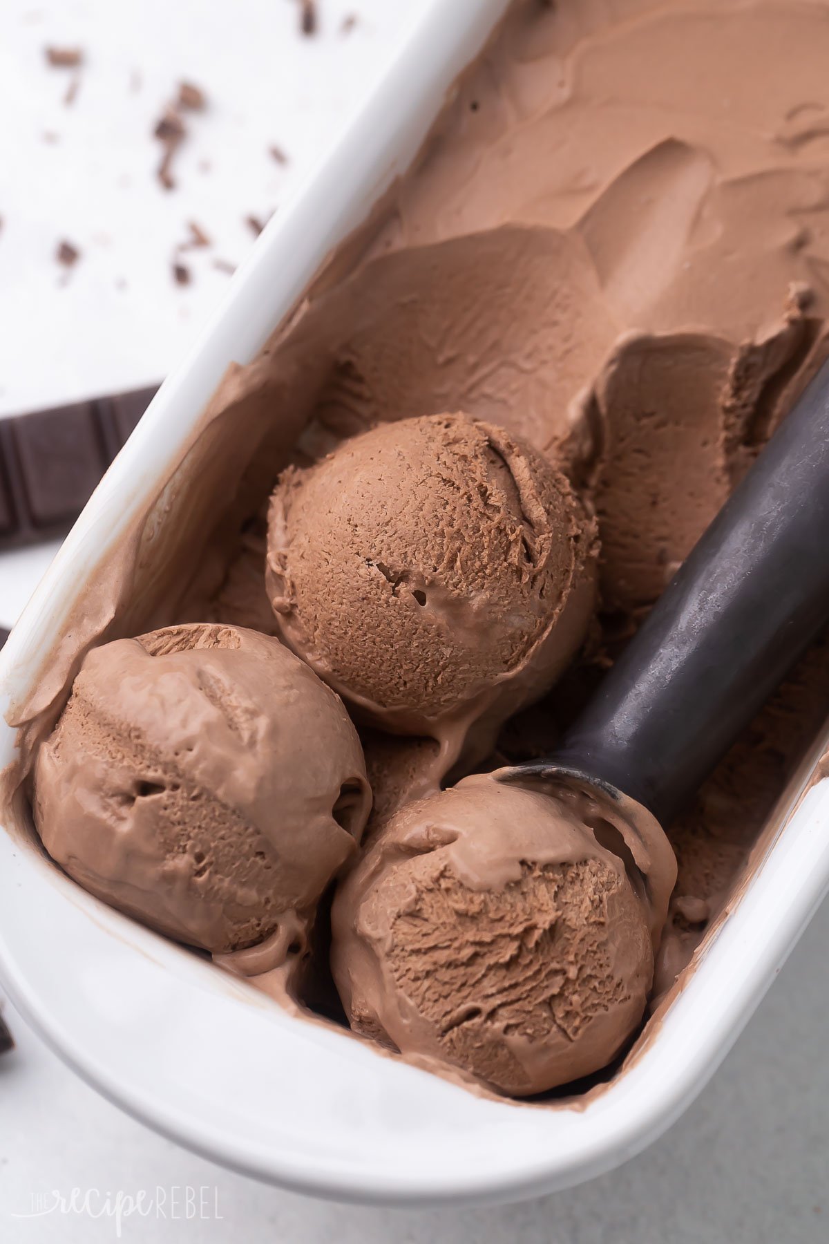 Top view of no churn chocolate ice cream in a white ice cream tub with an ice cream scoop in it. 