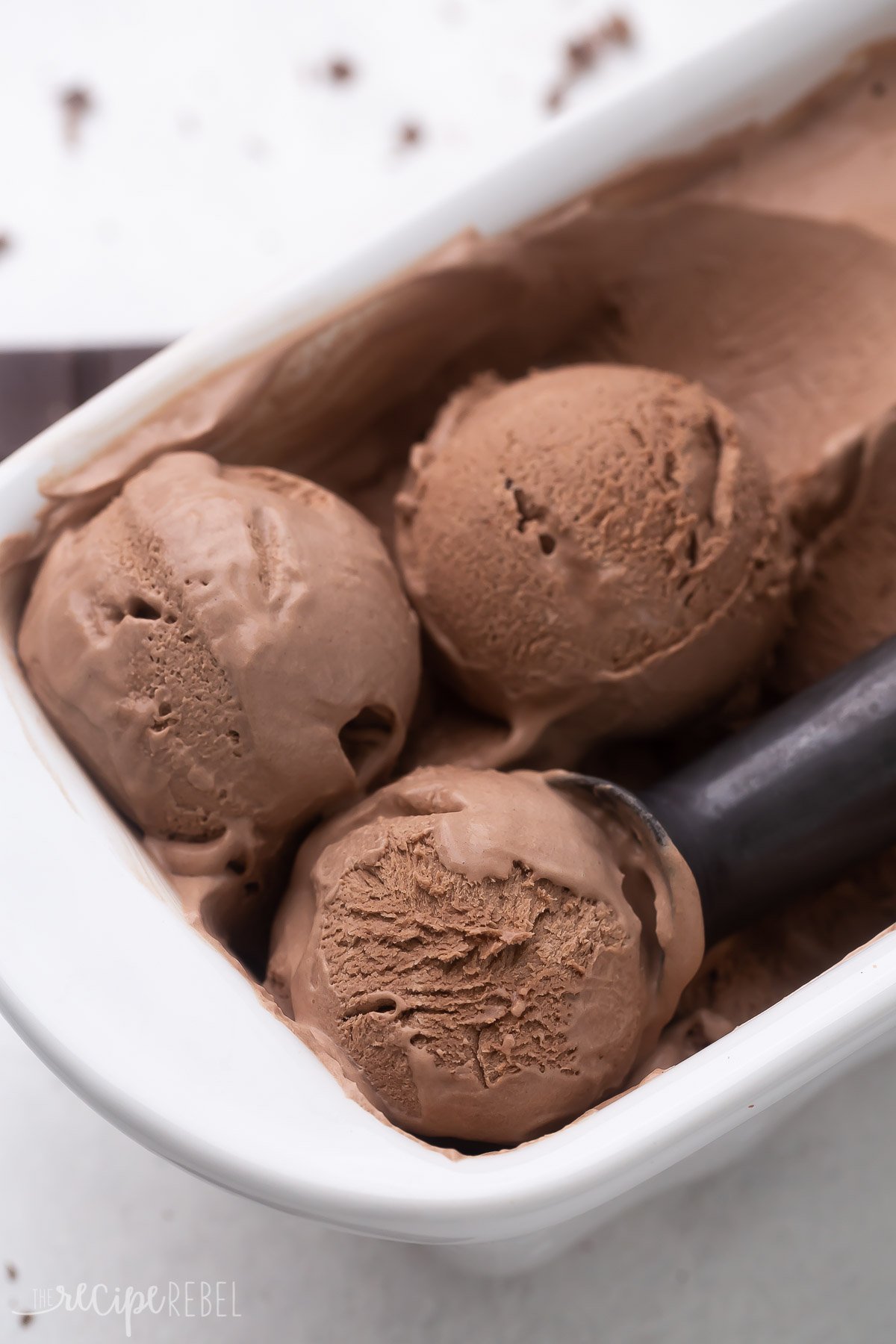 Top view of a white pan with chocolate ice cream in it, with an ice cream scoop scooping out some ice cream on top. 