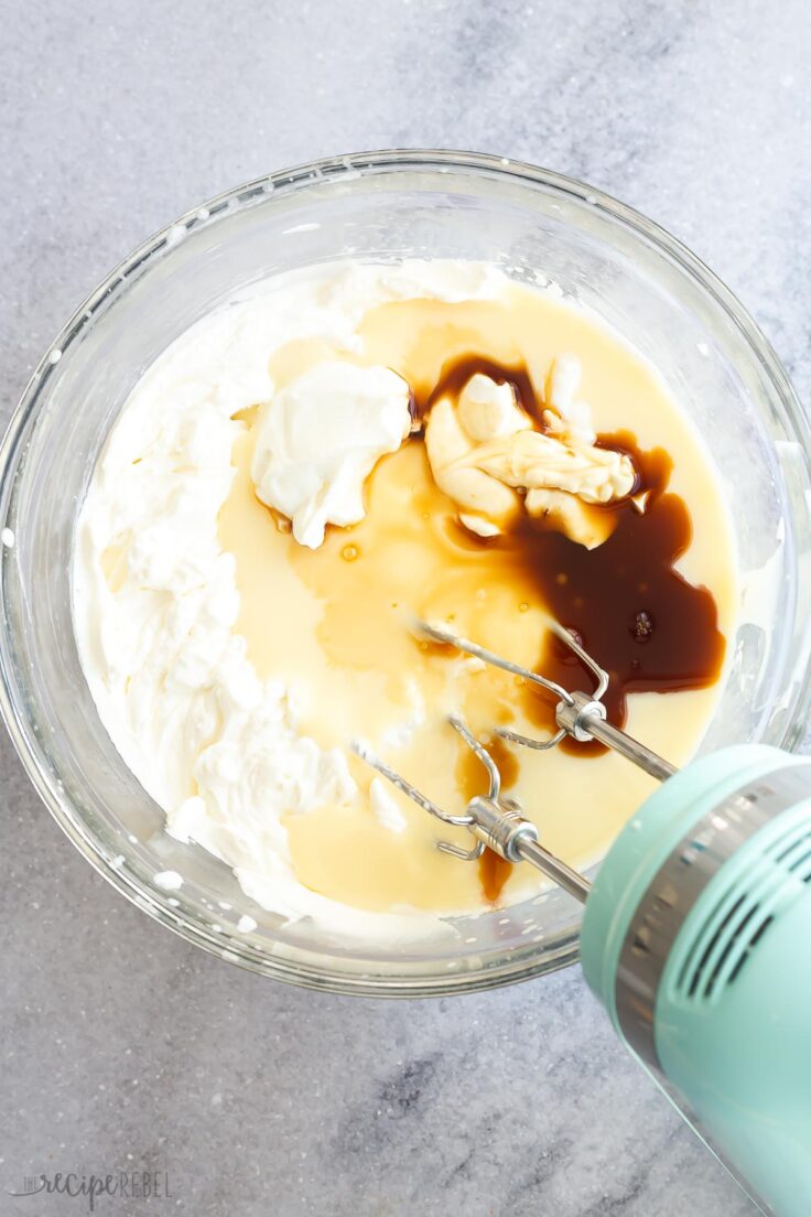 Top view of a glass mixing bowl with ingredients needed for No Churn Vanilla Ice Cream being whisked with an electric mixer. 