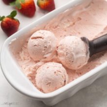 White dish filled with strawberry ice cream in it, being scooped out by an ice cream scoop.