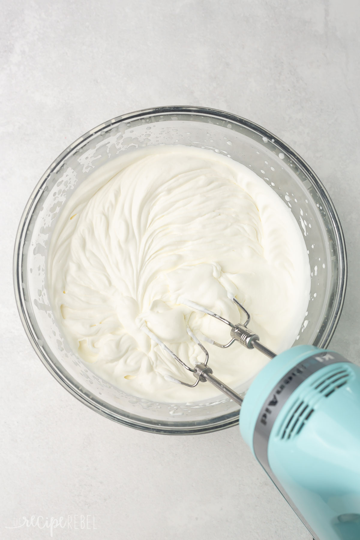 Top view of glass mixing bowl with heavy cream being whipped by an electic mixer.