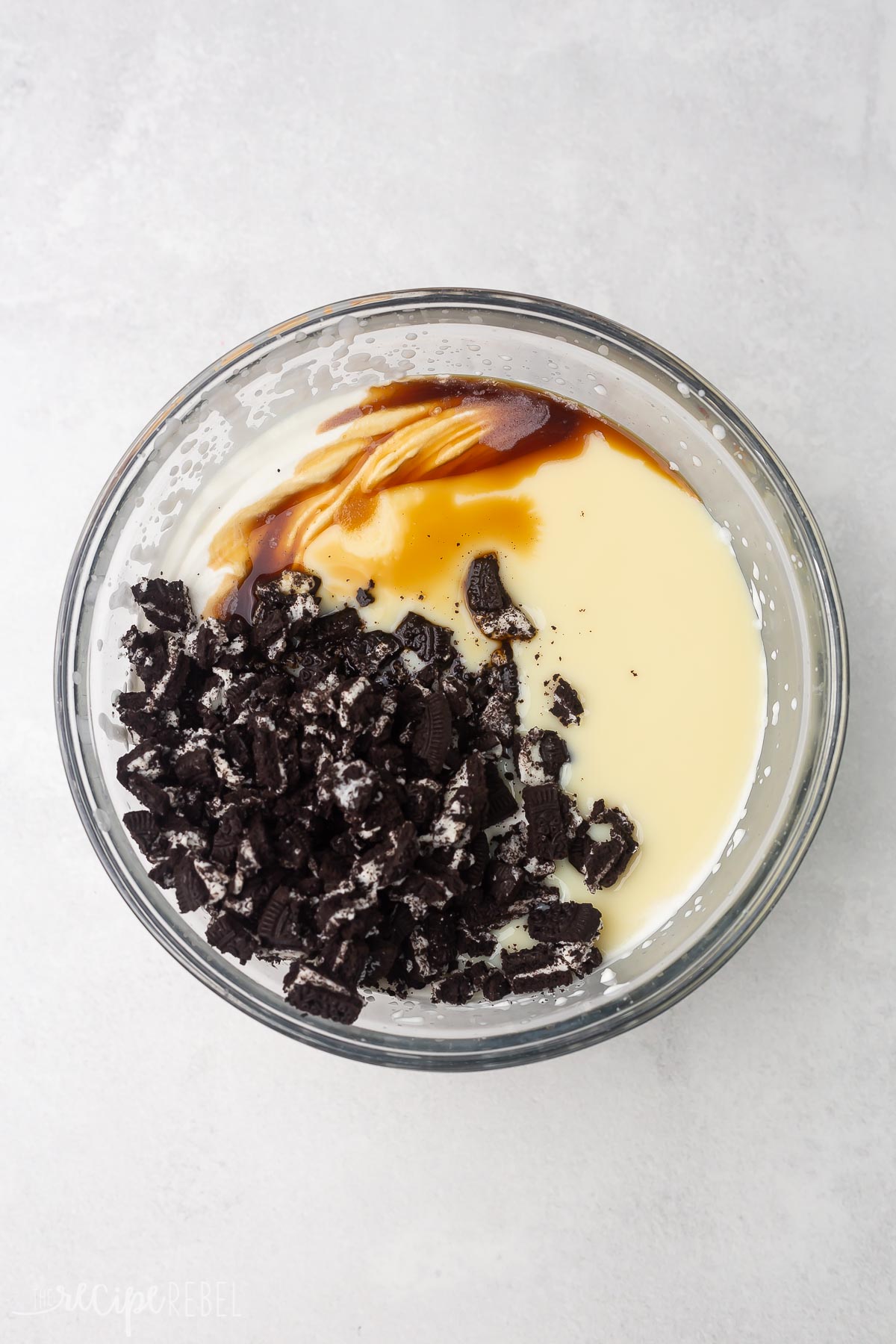 Top view of glass mixing bowl with whipped cream, vanilla, salt, and crushed Oreos in it, unmixed.