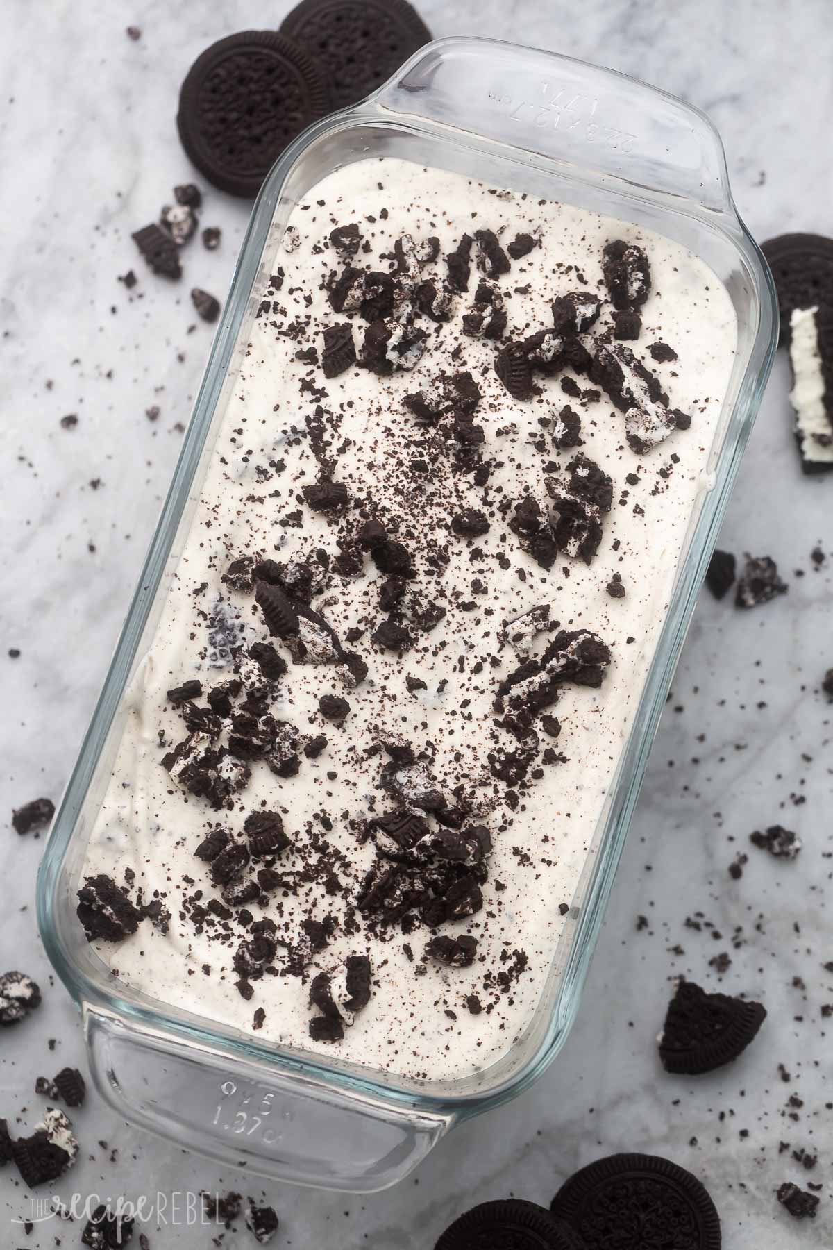 Top view of glass dish with No Churn Oreo Ice Cream in it, with Oreo pieces on top, surrounded by crushed Oreo bits on the worktop.