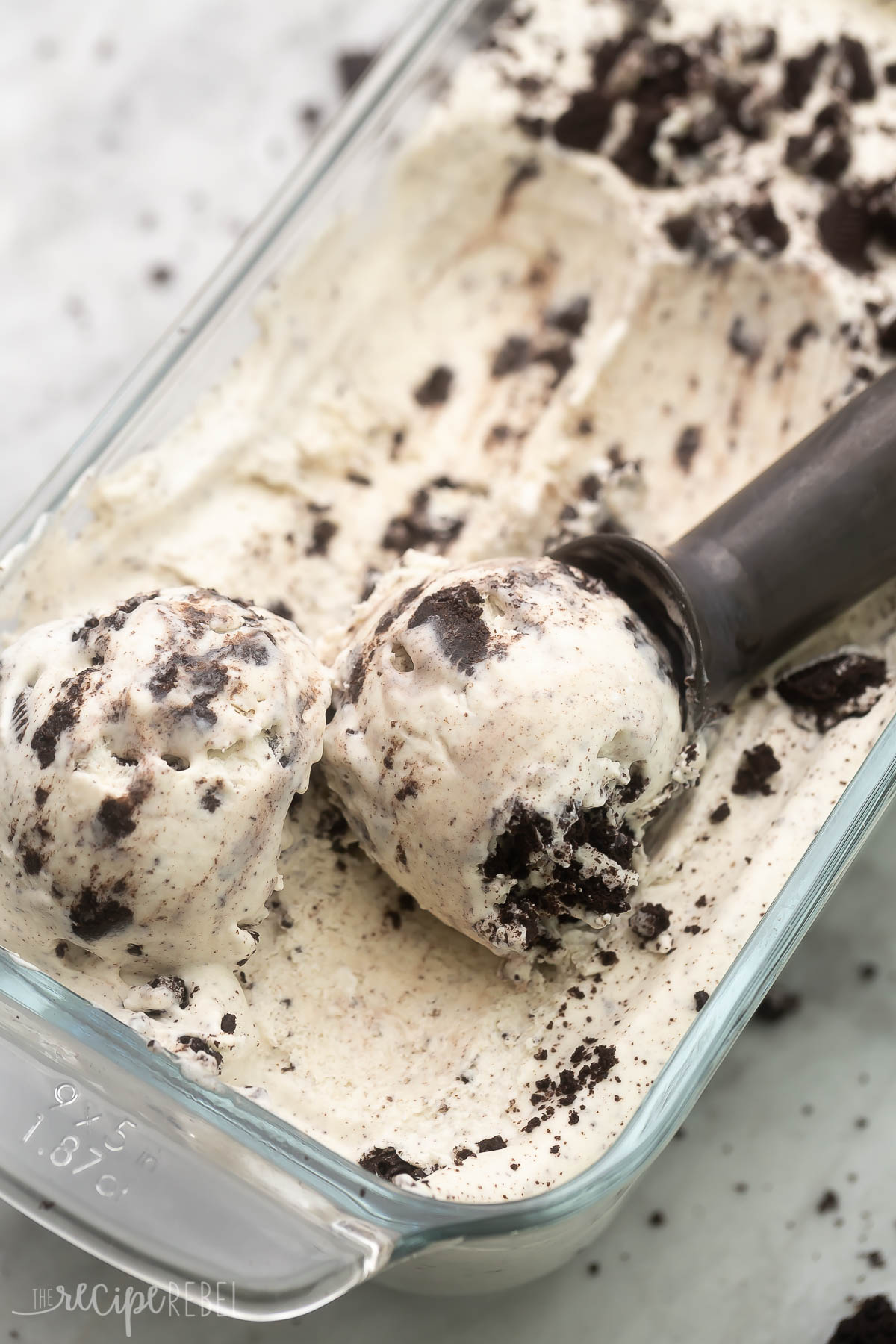 Close up of Ice Cream with Oreos in a glass dish being scooped with an ice cream scoop. 