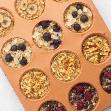 baked oatmeal cups in a muffin pan topped with fruit and chocolate chips.