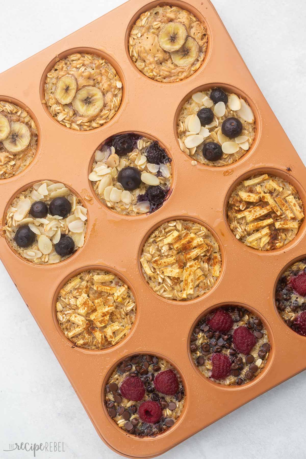 baked oatmeal cups in a muffin pan topped with fruit and chocolate chips.