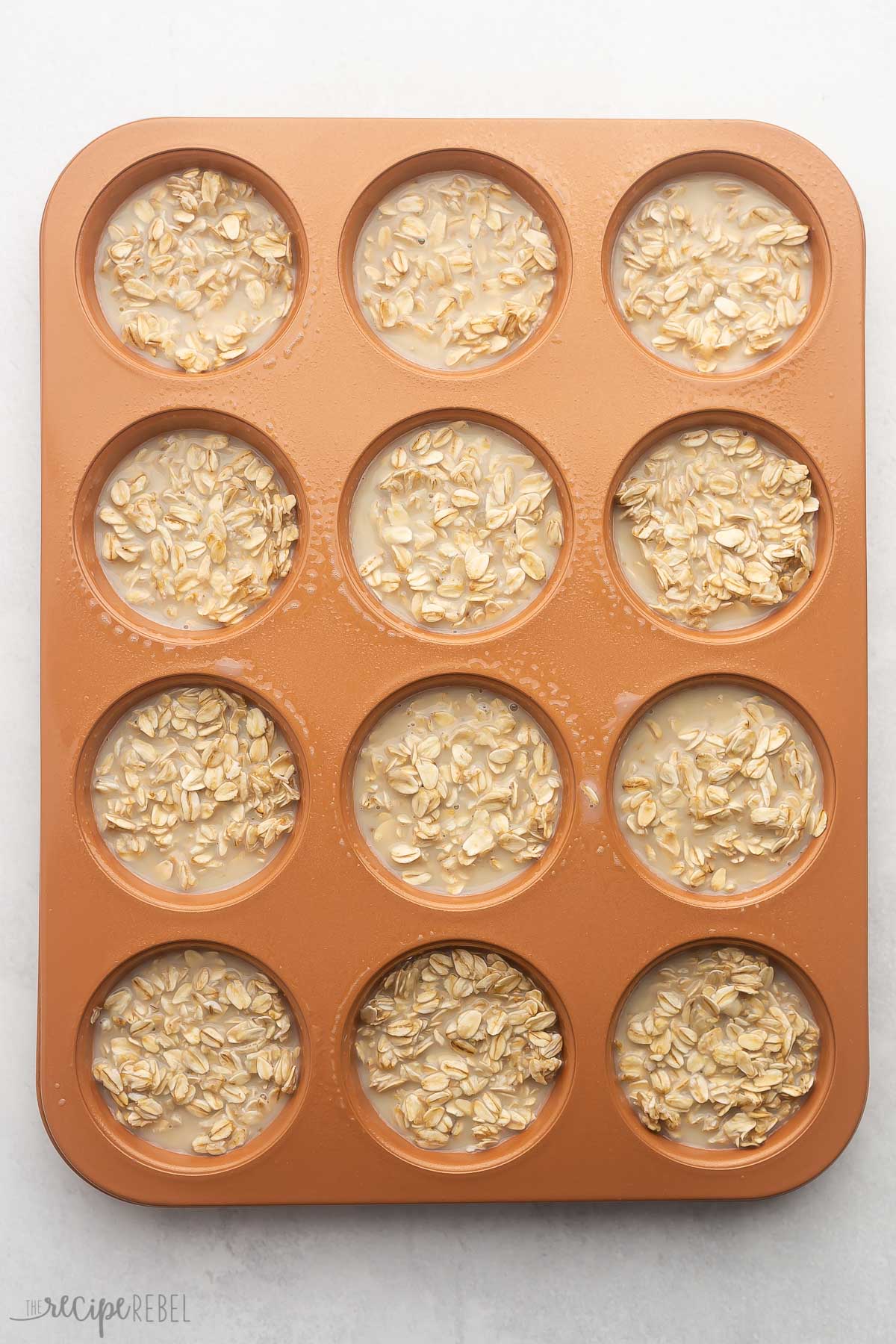 a muffin pan filled with unbaked oatmeal cup ingredients on grey surface.