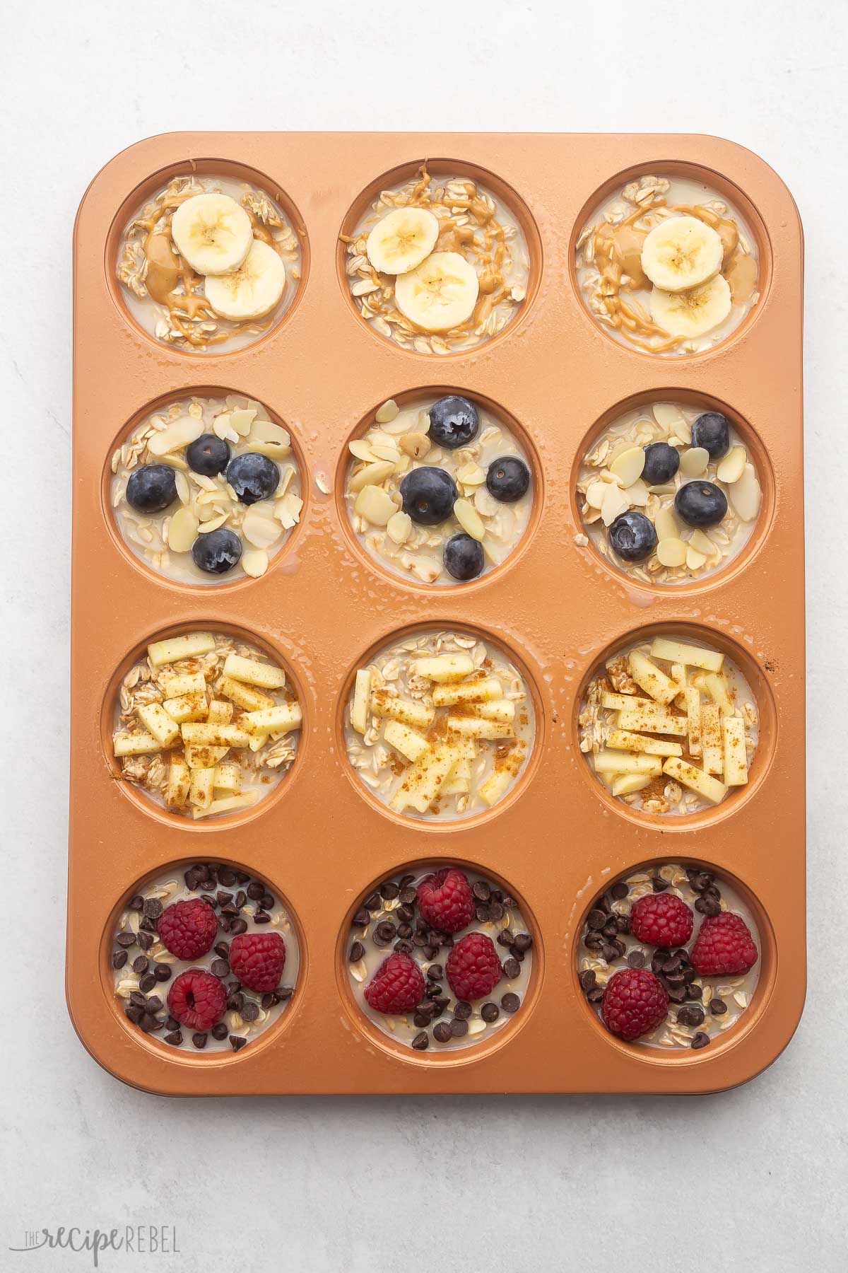unbaked oatmeal cups in a muffin pan topped with fruit and chocolate chips.