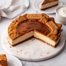 part of a biscoff cheesecake on a marble plate with pieces nearby.