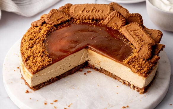 part of a biscoff cheesecake on a marble plate with pieces nearby.