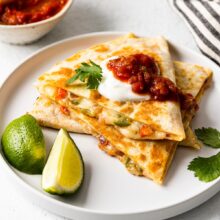 close up of cheese quesadillas on a white plate topped with salsa and sour cream.