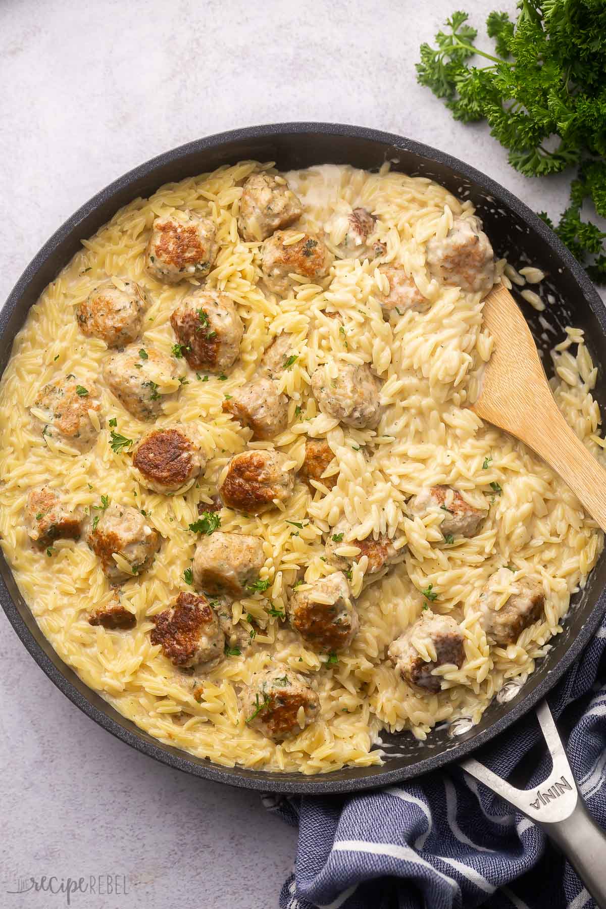 overhead view of cooked chicken meatballs with orzo in pan with wooden ladle.