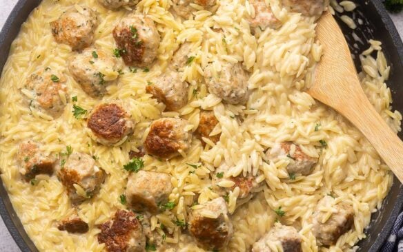 close up shot of cooked chicken meatballs and orzo in black frying pan.