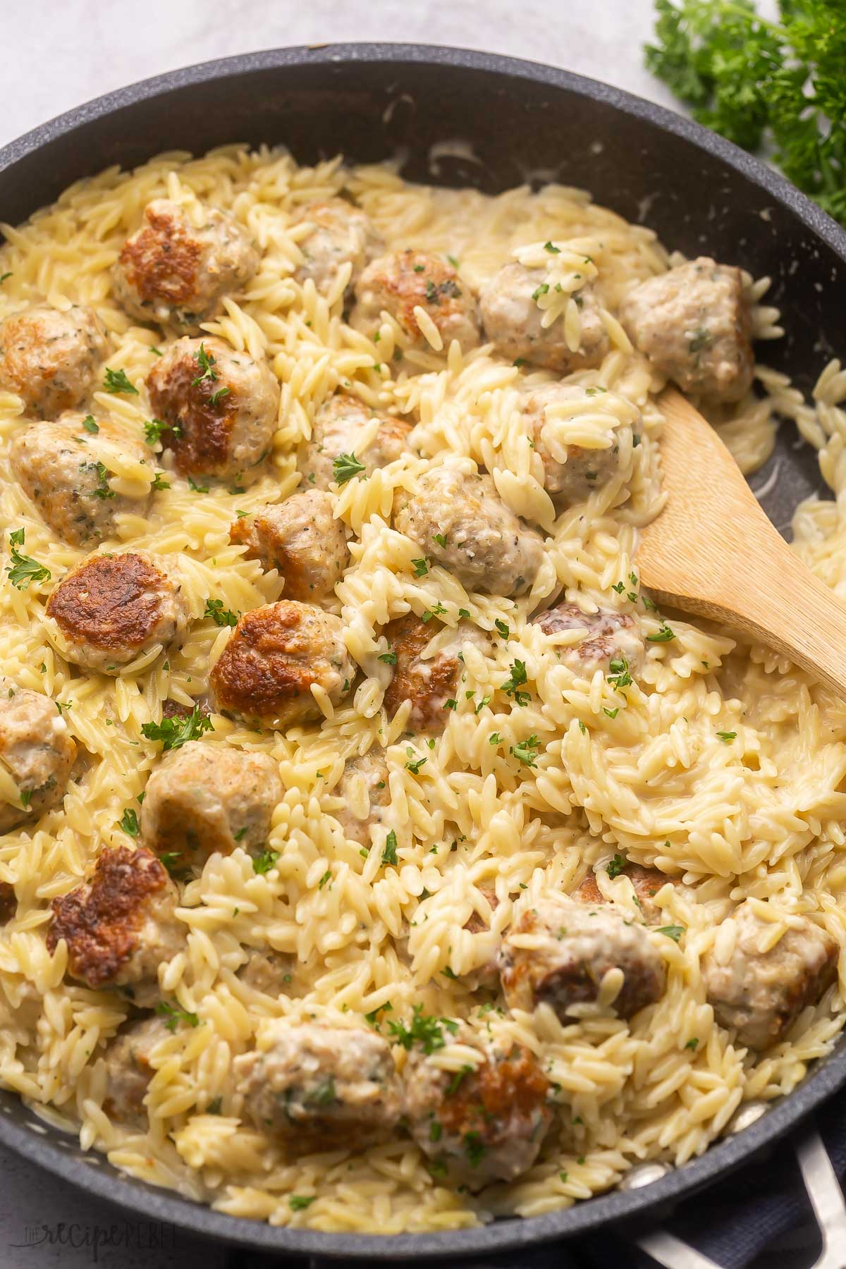 chicken meatballs and orzo in black pan with wooden ladle.