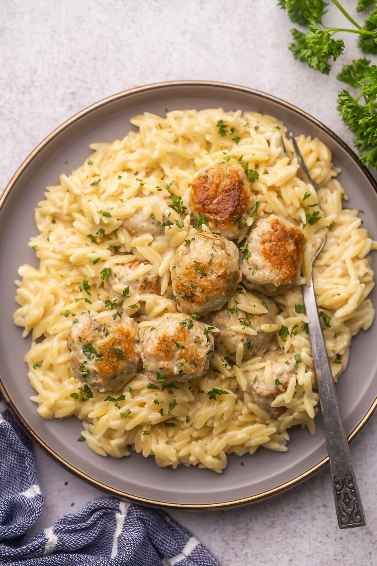 overhead shot of a grey plate full of chicken meatballs and orzo with a fork in it.