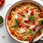 white pan full of tomato basil pasta with parmesan cheese on top and a wooden ladle.