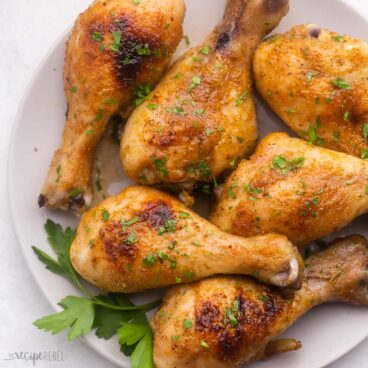 close up of a plate of chicken drumsticks garnished with parsley.