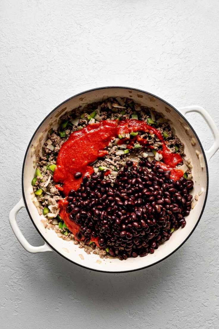 overhead shot of beans and sauce on top of other ingredients in pot.