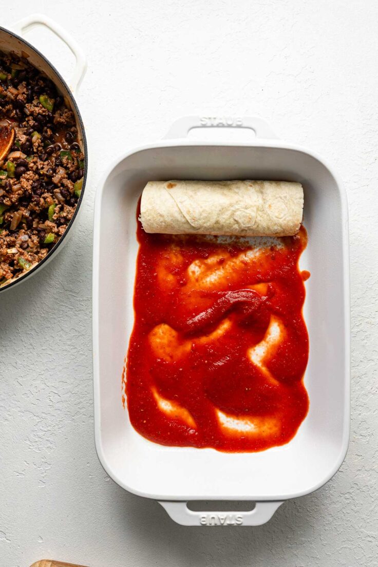 one rolled up beef taquito in a white baking dish on white surface.